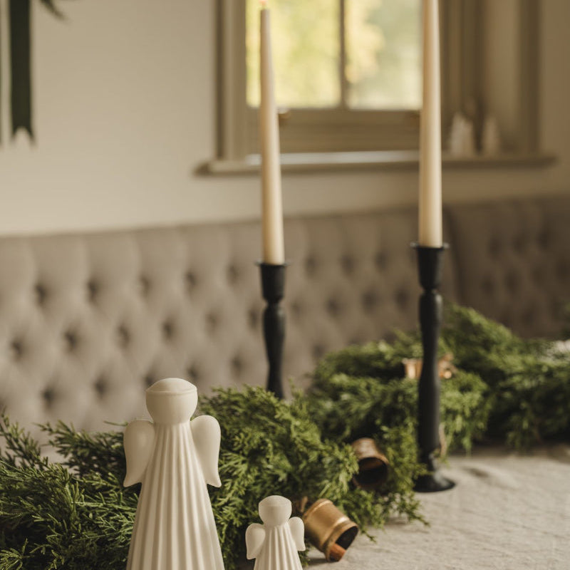 Decorative setup with candles, angel figurines, and greenery on a table.