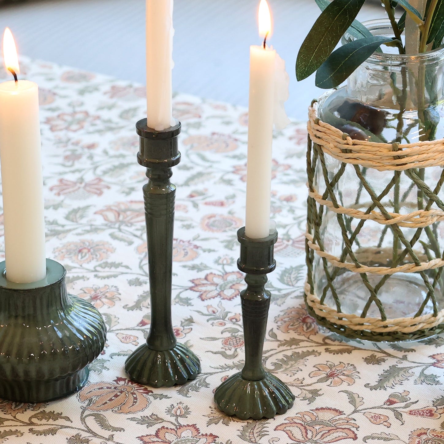 Decorative table setting with candles and greenery on a floral tablecloth.