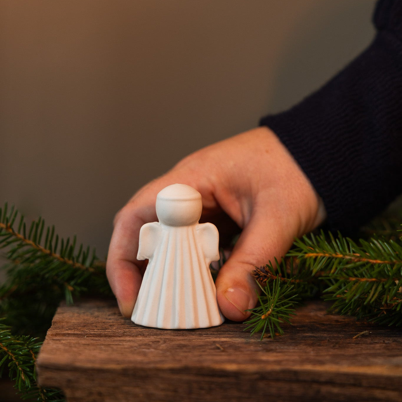 A hand holding a small ceramic angel figurine, with a blurred background suggesting indoor setting, possibly during Christmas decoration.