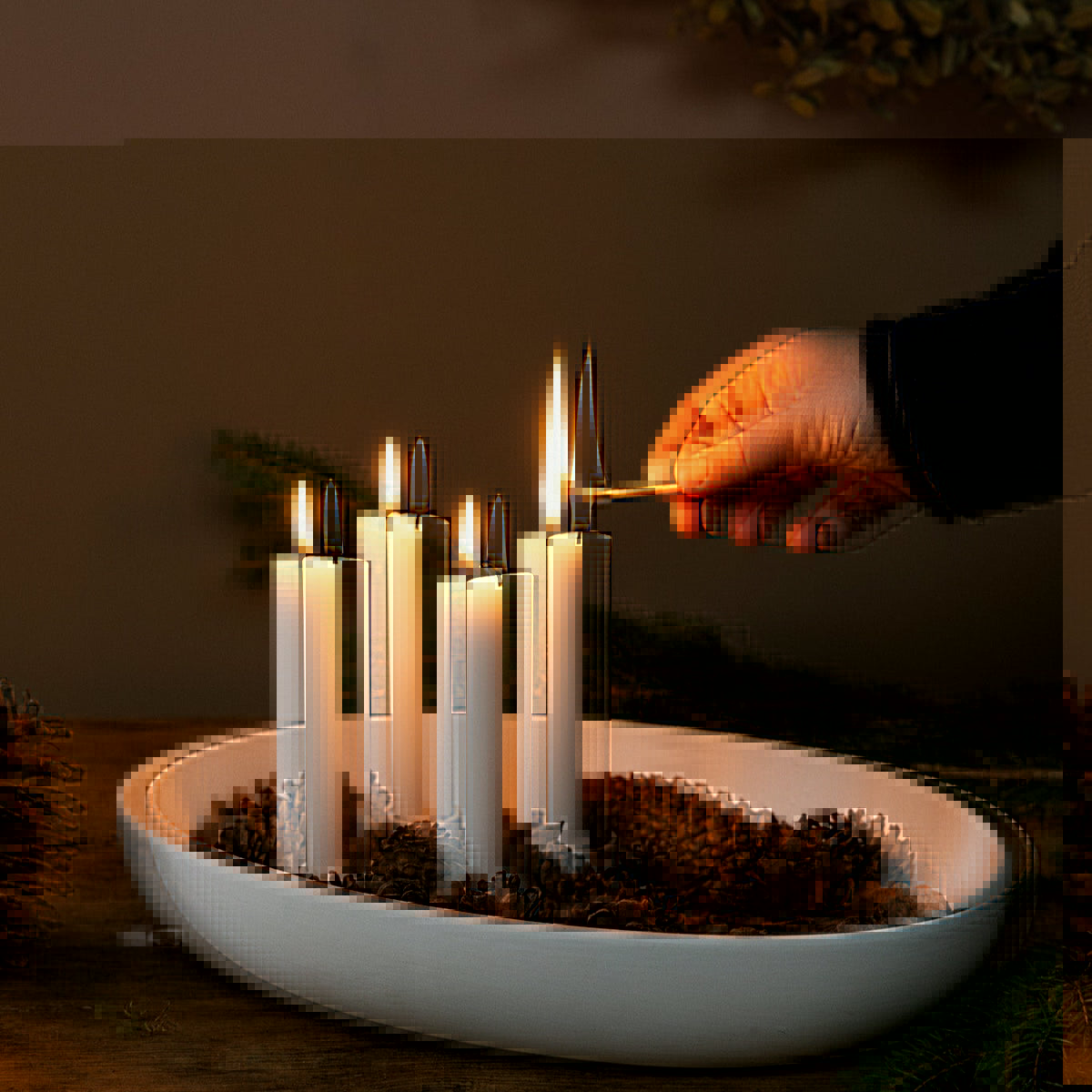 A hand is shown lighting a candle in a white matte candle holder, which is placed on a wooden surface. The holder contains four candles, and there is a bowl of decorative pine needles nearby.