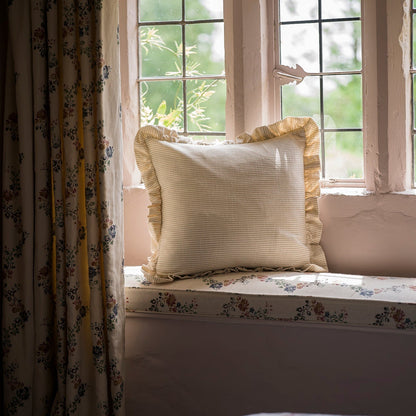 Decorative pillow on a window seat with floral curtains and a view of greenery outside.