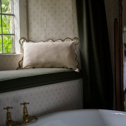 Window seat with a pillow, patterned wallpaper, and a window with greenery outside.