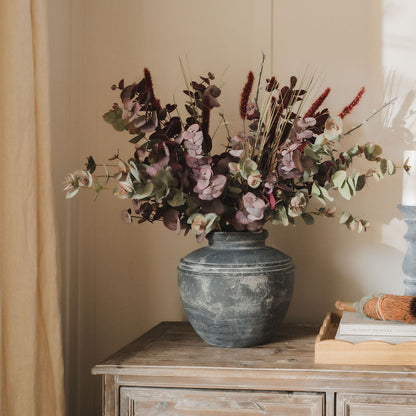 Decorative vase with flowers on a wooden dresser against a beige wall