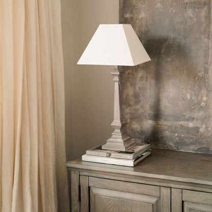 Tall distressed wood table lamp with a classic tapered white shade, styled on stacked books atop a rustic wooden console table against a textured neutral wall