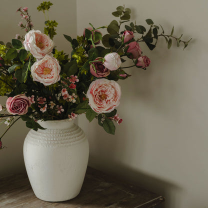 White vase with pink and green flowers against a plain wall