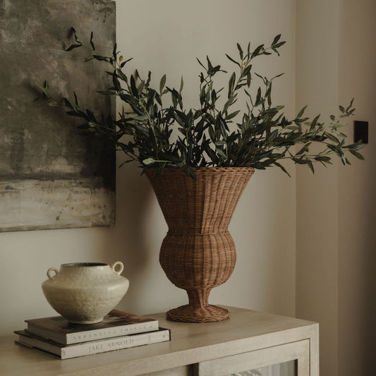 Decorative setup with a wicker vase, ceramic pot, and books on a shelf against a neutral wall.