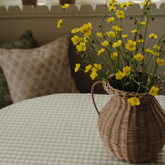 Wicker basket with yellow flowers on a checkered tablecloth, with plants in the background.