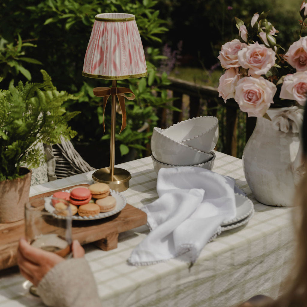 Outdoor setting with a table featuring a lamp, flowers, and macarons in a garden.