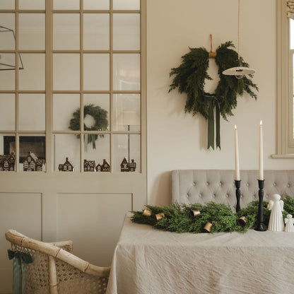 Dining room with a wreath on the wall, table with greenery, and candles.