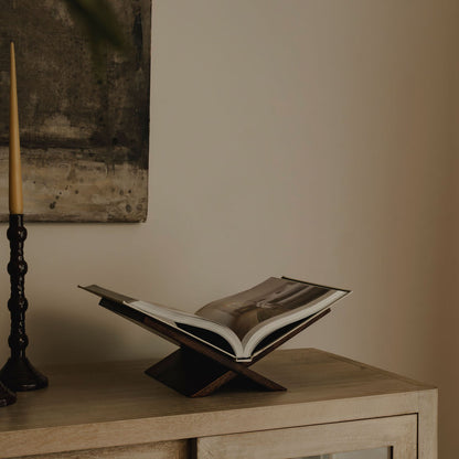 Open book on a wooden stand with a candle and painting in the background