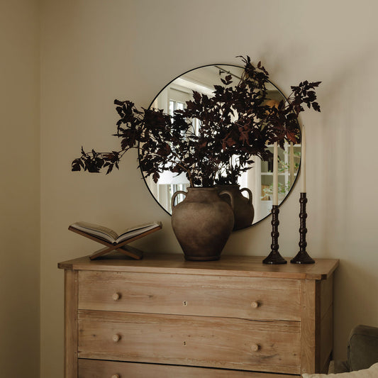 Large rustic stoneware vase styled with dark faux foliage on wooden chest of drawers
