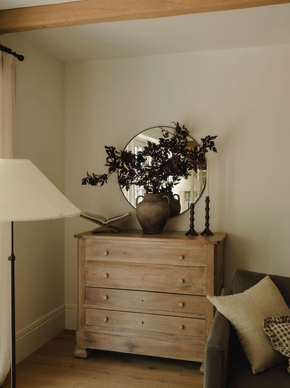 Large rustic stoneware vase styled with dark faux foliage on wooden chest of drawers