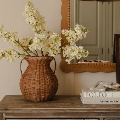 Wicker vase with white flowers on a wooden surface next to a mirror