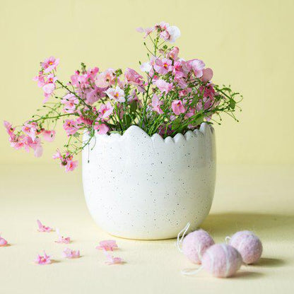 White ceramic planter with pink flowers on a light yellow background